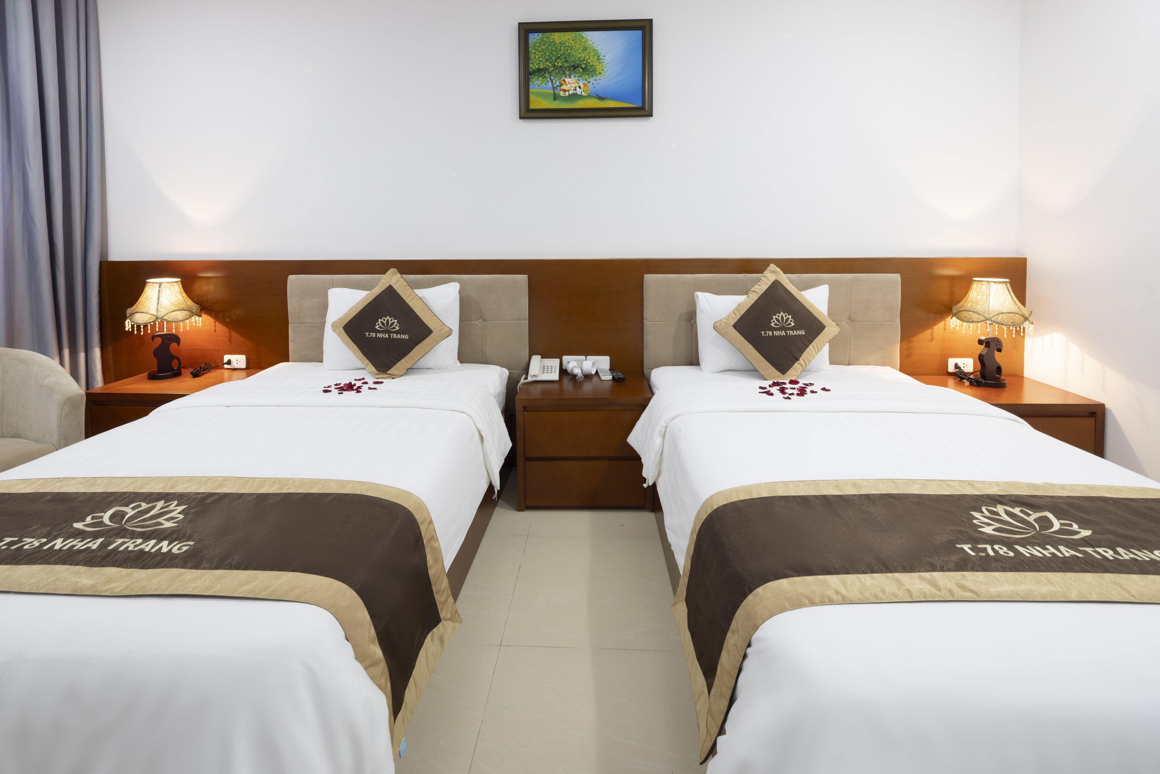 A hotel room with two beds, each with a headboard, bedside tables, lamps, and a framed picture on the wall.