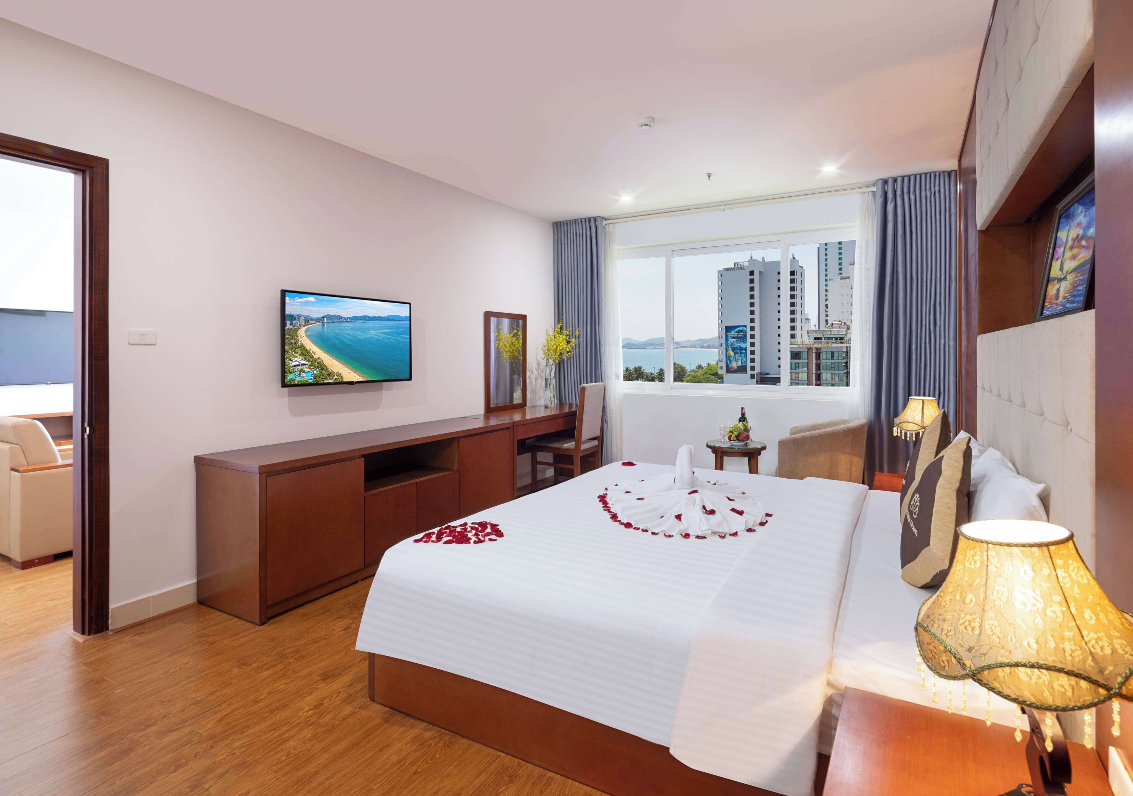 Une chambre d’hôtel comprenant un lit, une télévision, un bureau, une chaise, une fenêtre donnant sur la ville et un balcon.