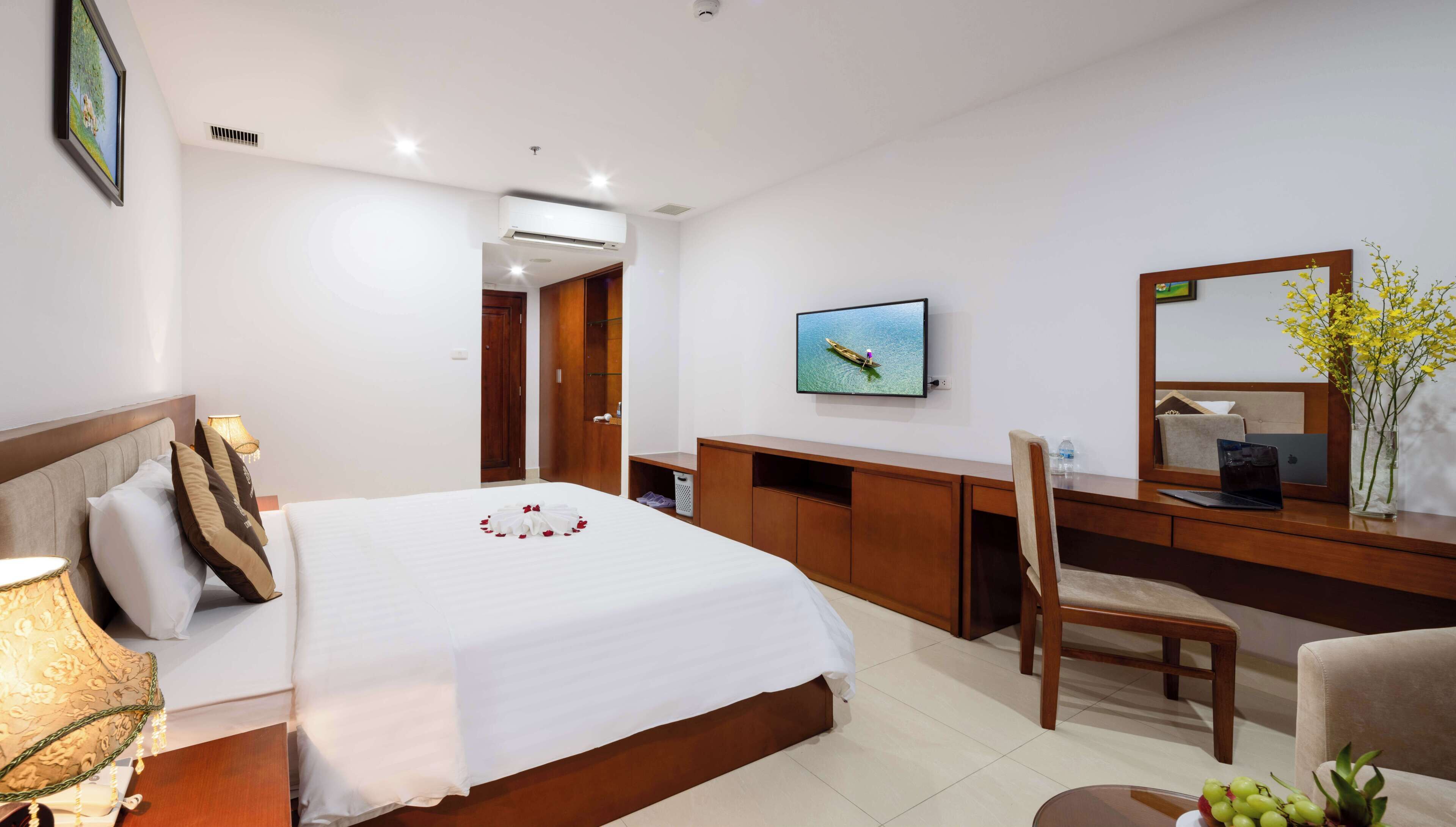 A hotel room with a bed, desk, chair, TV, and a mirror.