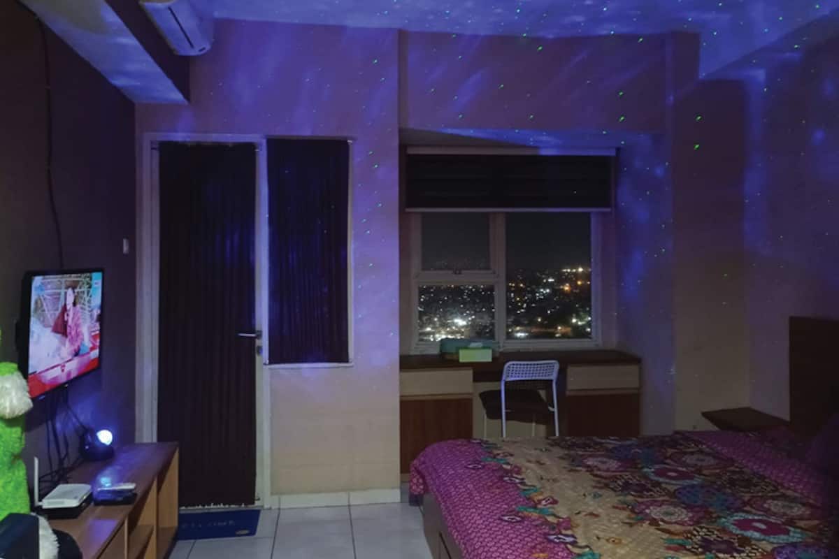Ein Schlafzimmer mit Bett, Schreibtisch, Stuhl, Fernseher und einem Fenster mit Blick auf die Stadt.
