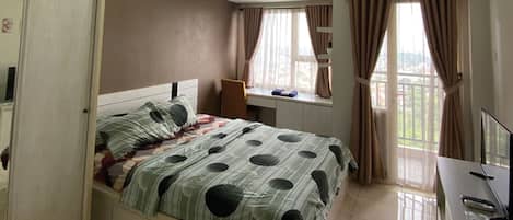 A bedroom with a bed, a desk, and a window with curtains.