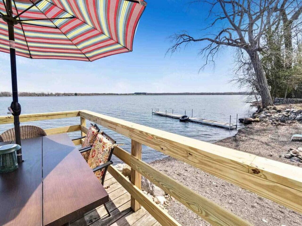 Um deck de madeira com mesa e cadeiras, com vista para um lago tranquilo e um píer.