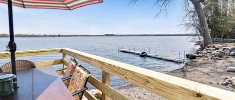 Um deck de madeira com mesa e cadeiras, com vista para um lago tranquilo e um píer.