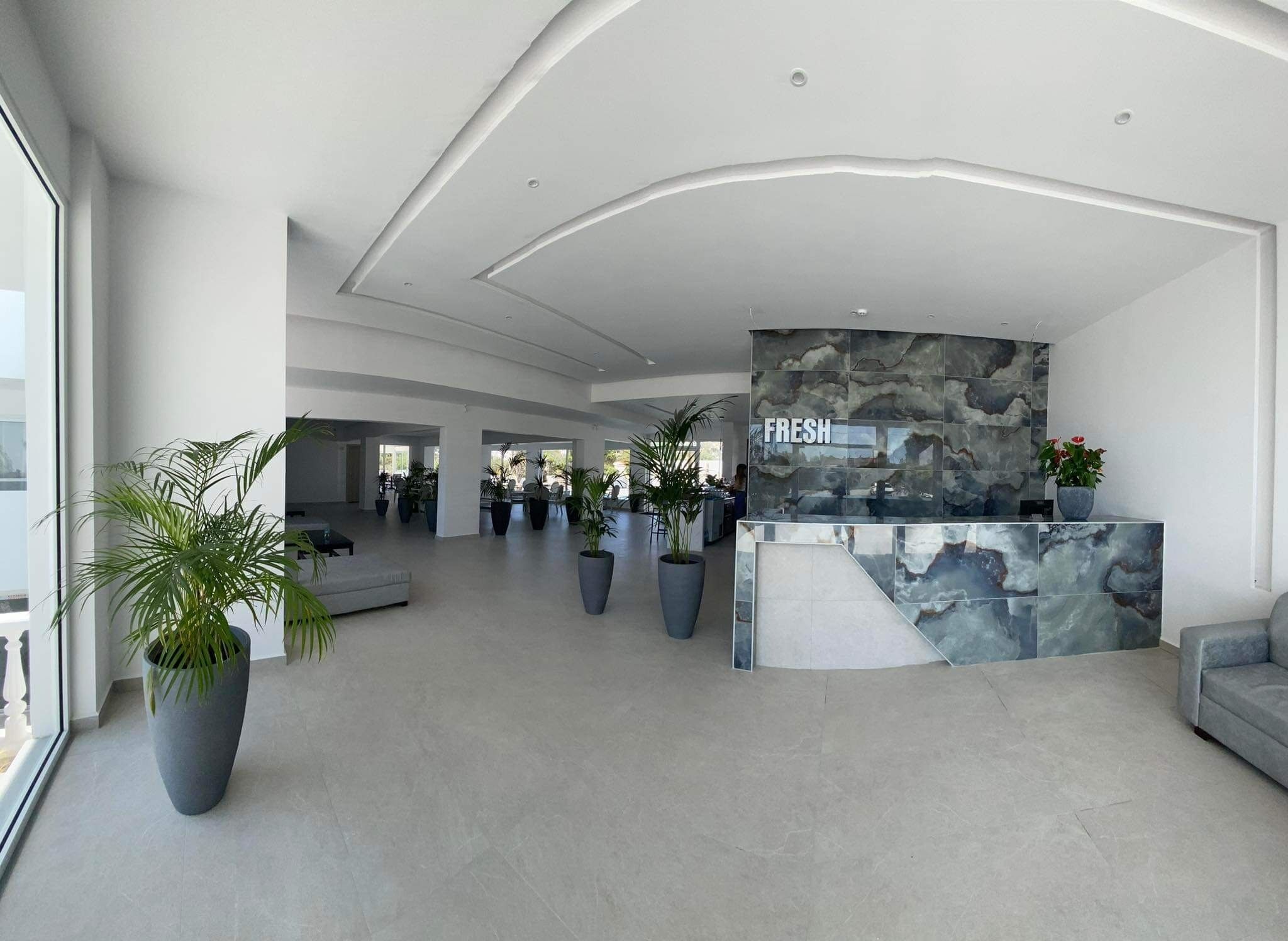 Een ruime lobby met een receptiebalie, grote potplanten en een modern architectonisch ontwerp.