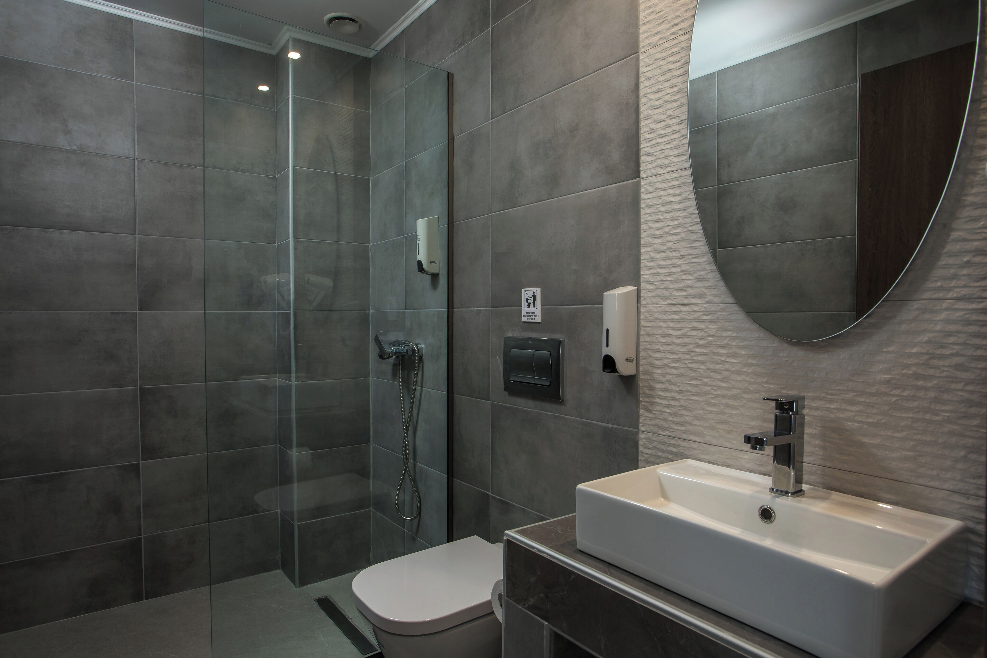 A modern bathroom with a glass-enclosed shower, a white toilet, and a rectangular sink with a mirror above it.