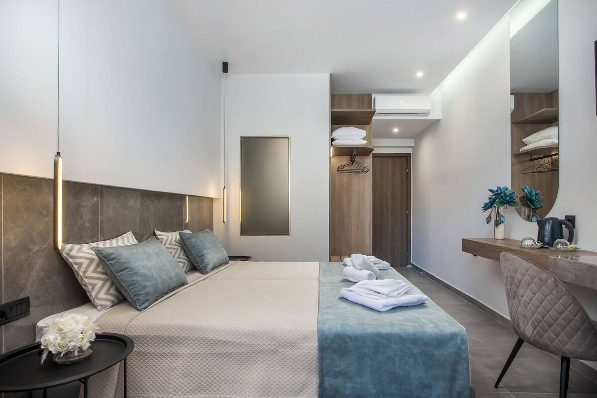 Une chambre d’hôtel moderne avec un grand lit, une table de chevet, une chaise, un bureau et un miroir.