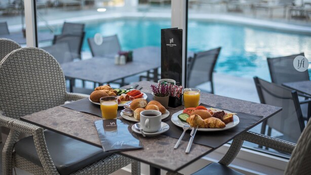 A breakfast setup with croissants, fruits, and juice on a table by a poolside. - Fresh hotel rhodes (Rhodes)