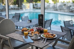 Disposição para o café da manhã com croissants, frutas e suco em uma mesa à beira da piscina.