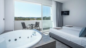 A modern hotel room with a large bathtub, a sofa bed, a TV, and a balcony with a view of the countryside. - Fresh hotel rhodes (Rhodes)
