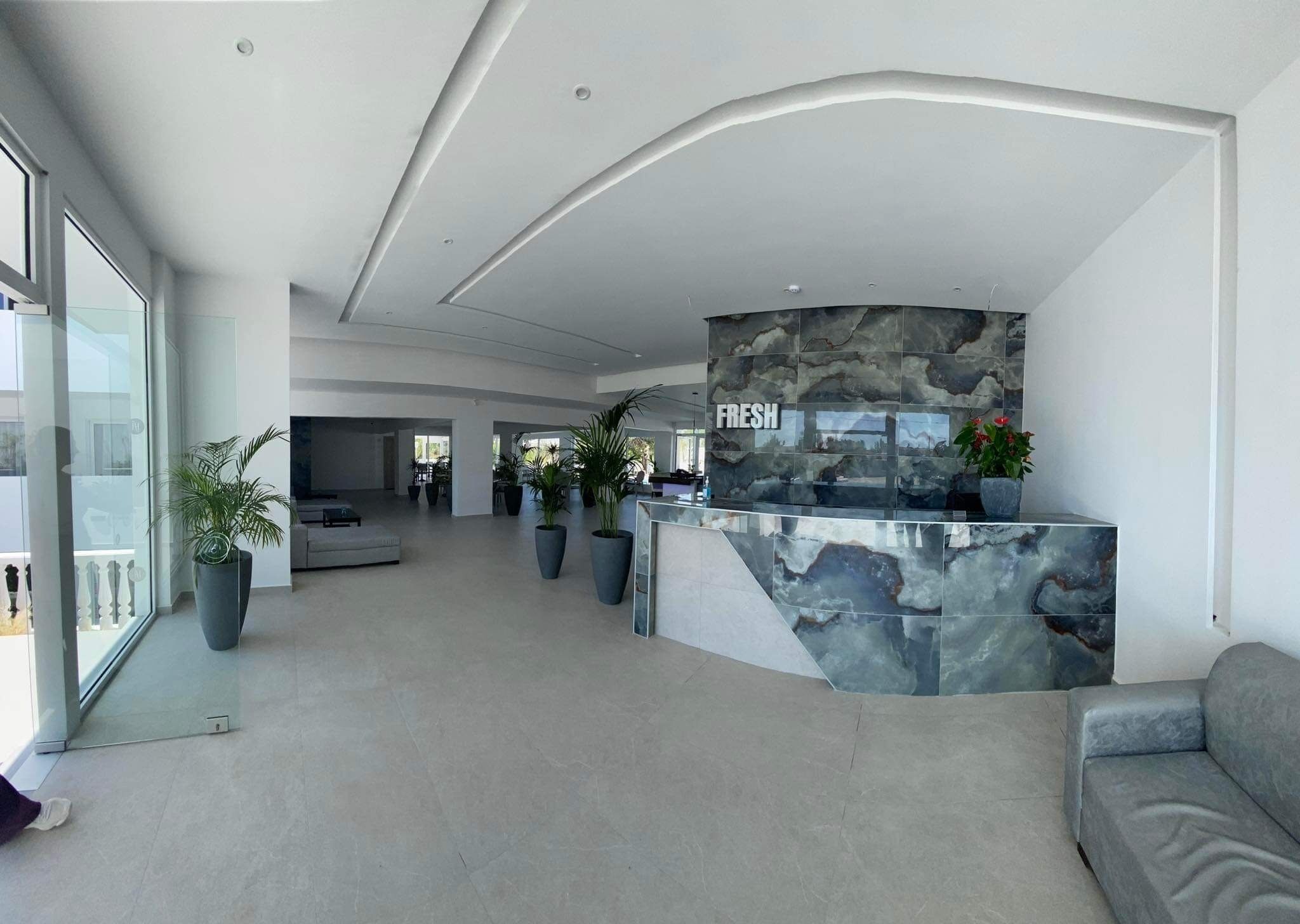 Un hall d’entrée spacieux, doté d’un comptoir d’accueil incurvé, de grands pots de plantes et d’un aménagement intérieur moderne.