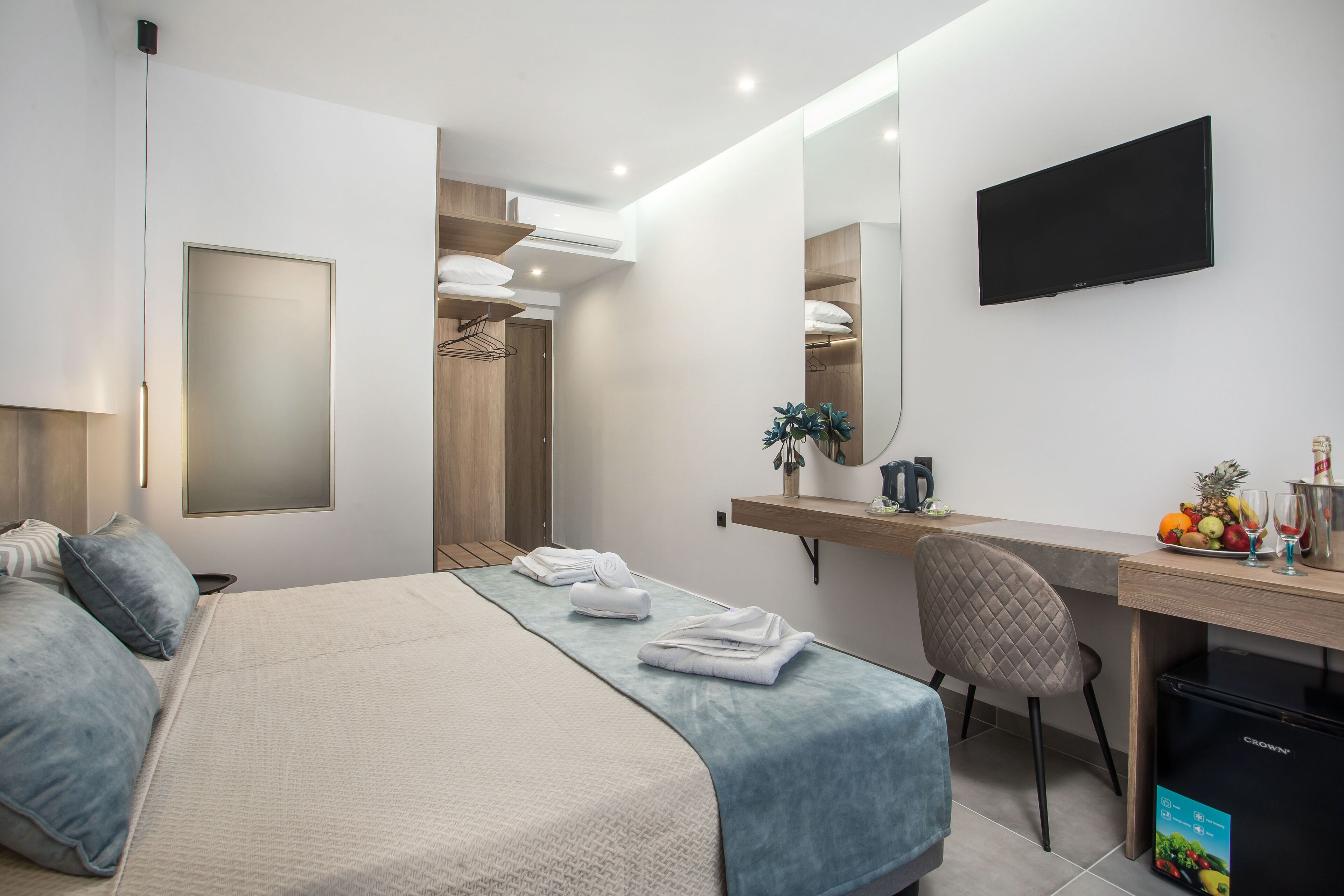 A modern hotel room with a large bed, a desk with a computer, a flat-screen TV, and a small refrigerator.