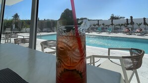 A glass of iced tea with a straw on a table by a poolside with lounge chairs and umbrellas. - Fresh hotel rhodes (Rhodes)