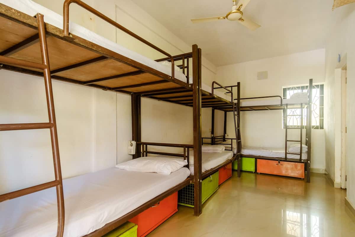 Ein Schlafsaalzimmer mit Etagenbetten, Deckenventilator und einem Fenster mit Gitterstäben.