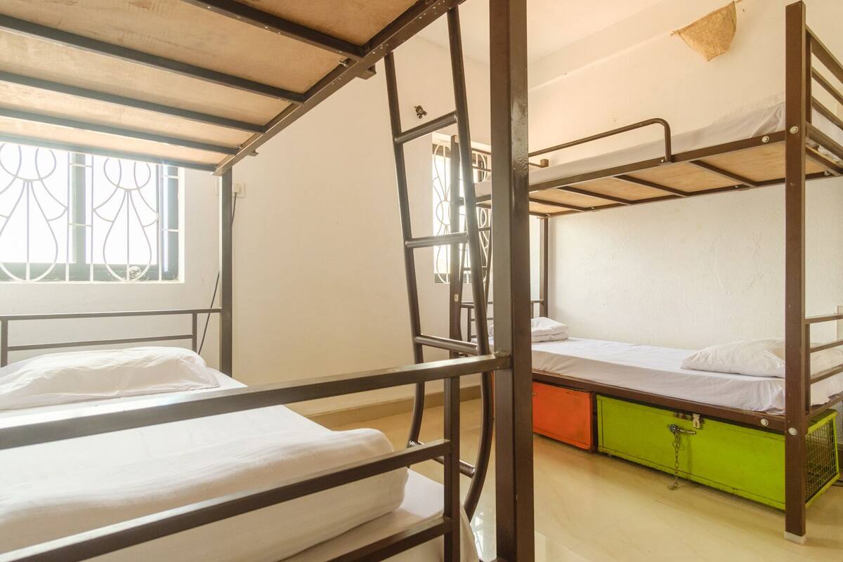 Ein Schlafsaalzimmer mit Etagenbetten, einem Fenster mit Ziergitter und einem grünen Schrank.