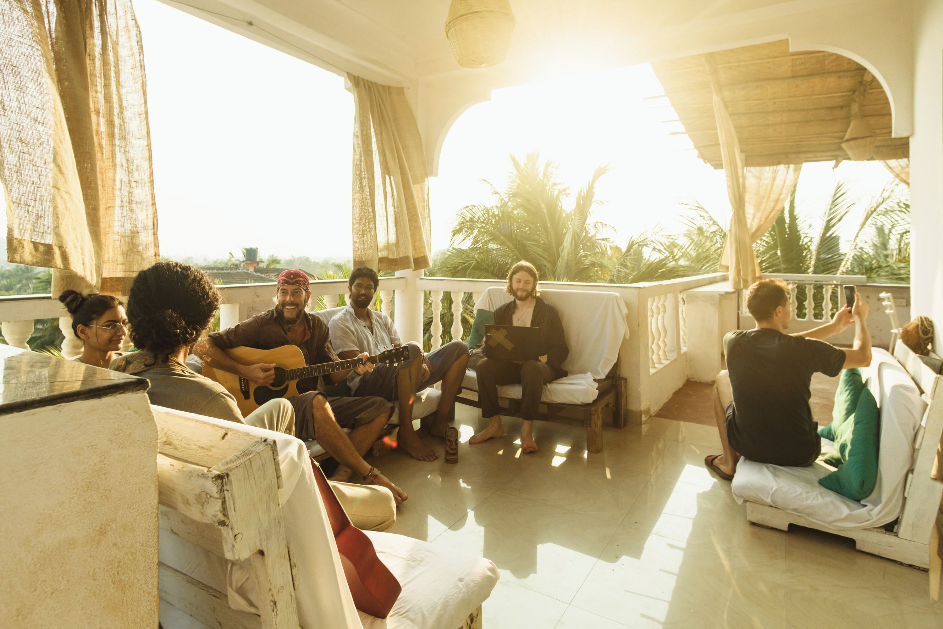 A group of people sitting on a terrace with a view of palm trees and a building in the background.