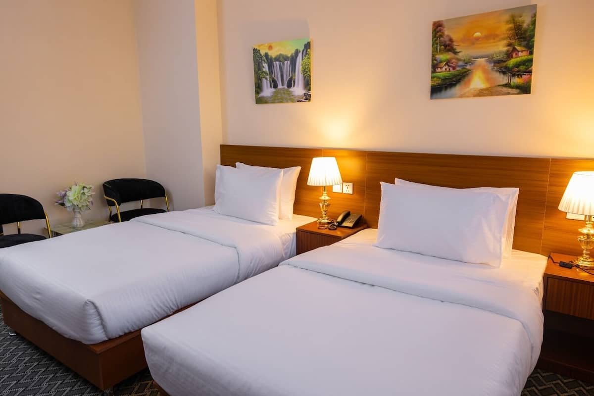 Hotellihuone, jossa on kaksi sänkyä, puinen pääty, yöpöytävalaisimet, puhelin ja kaksi taulua seinällä.