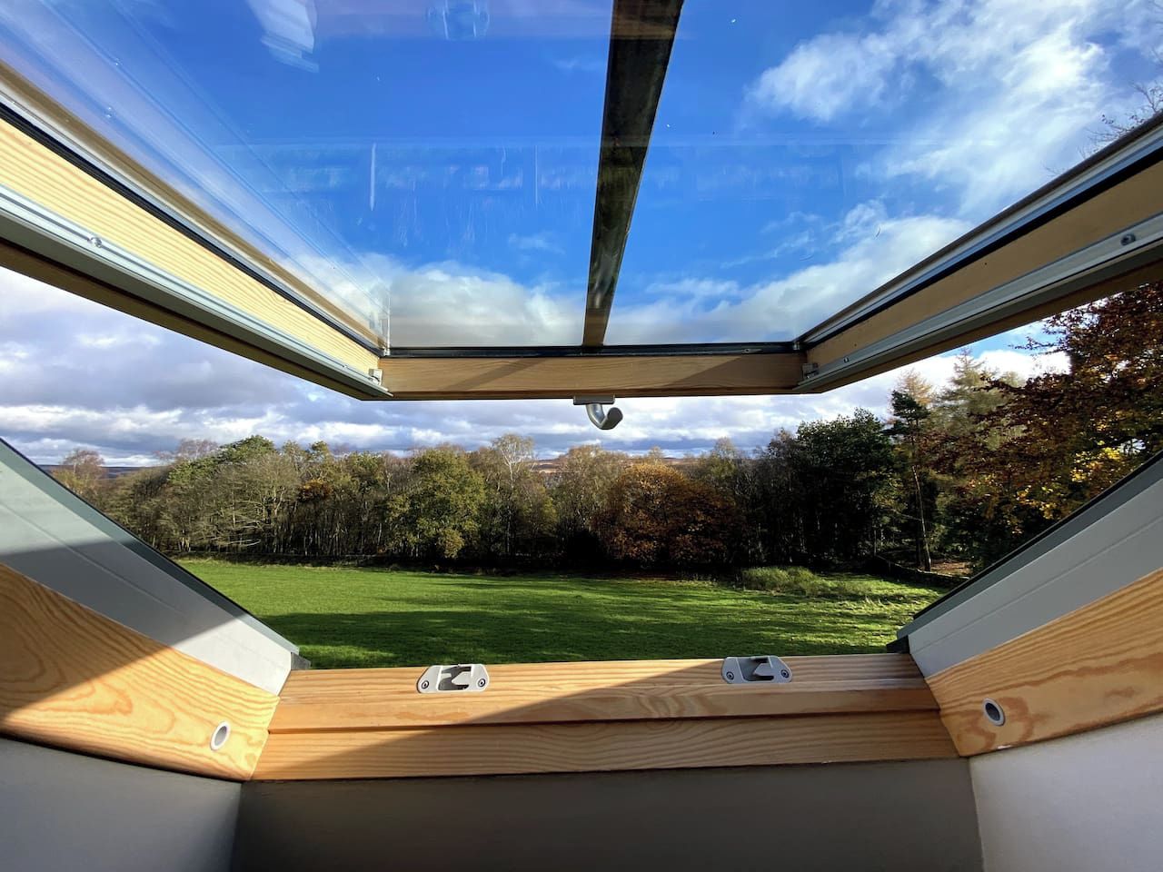 A room with a skylight, a view of a green field, and trees in the background.