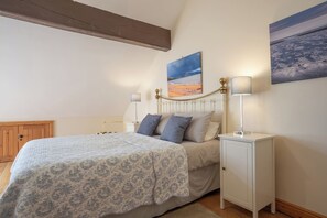 A bedroom with a bed, bedside tables, a nightstand, a wooden wardrobe, and two wall-mounted paintings.
