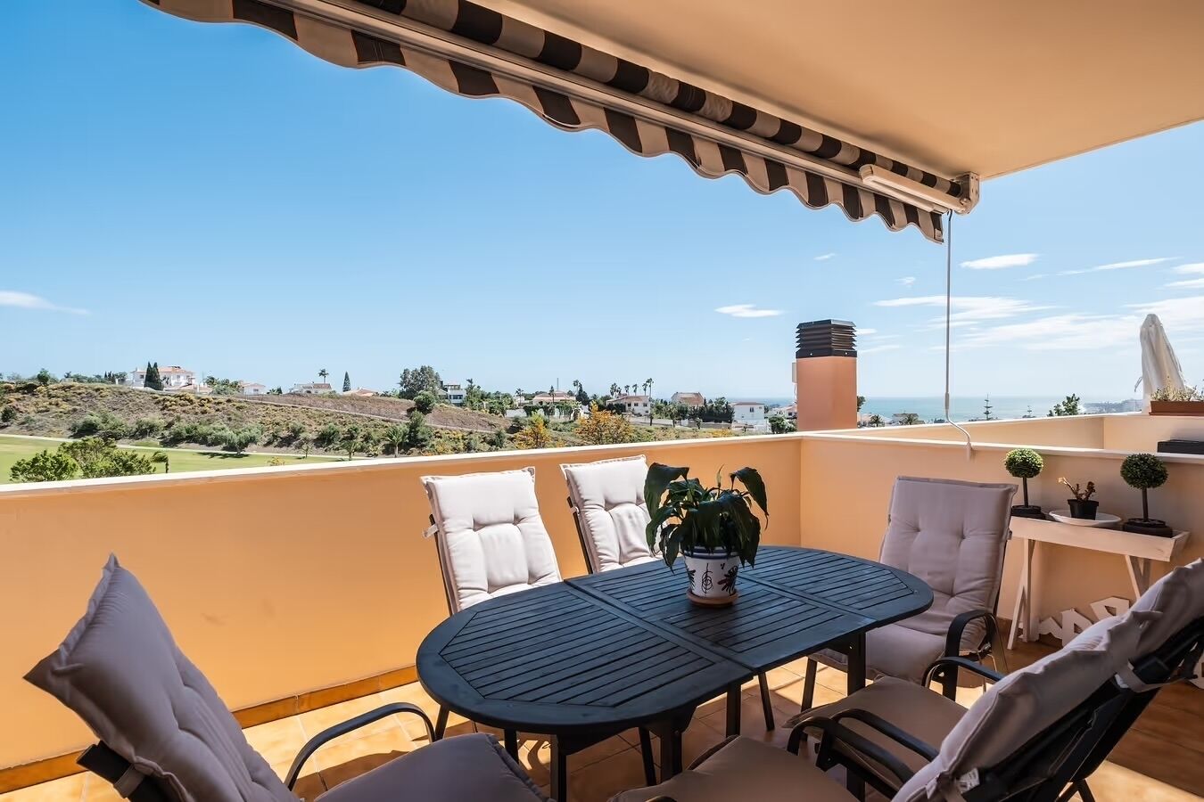 Ein Balkon mit Tisch und Stühlen, einer Topfpflanze und Blick auf die Landschaft.