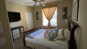 A bedroom with a bed, a ceiling fan, a TV mounted on the wall, a window with curtains, and a door. - Private access, private room, private bathroom (Goodyear)