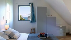 A bedroom with a bed, a window with a view, a dresser, and a small stool.