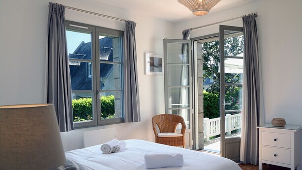 A bedroom with a bed, a chair, a nightstand, and a window with curtains.