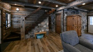 A rustic interior with a wooden staircase, stone walls, a wooden cabinet, and a blue pet bed.