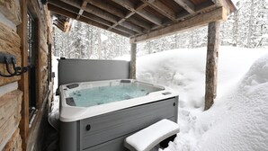 A hot tub in a wooden cabin with a bench in front, surrounded by snow.