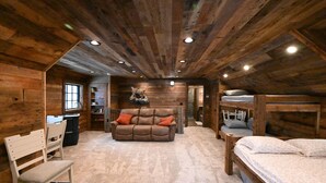 A log cabin interior with a sofa, bunk beds, a desk, and a chair.