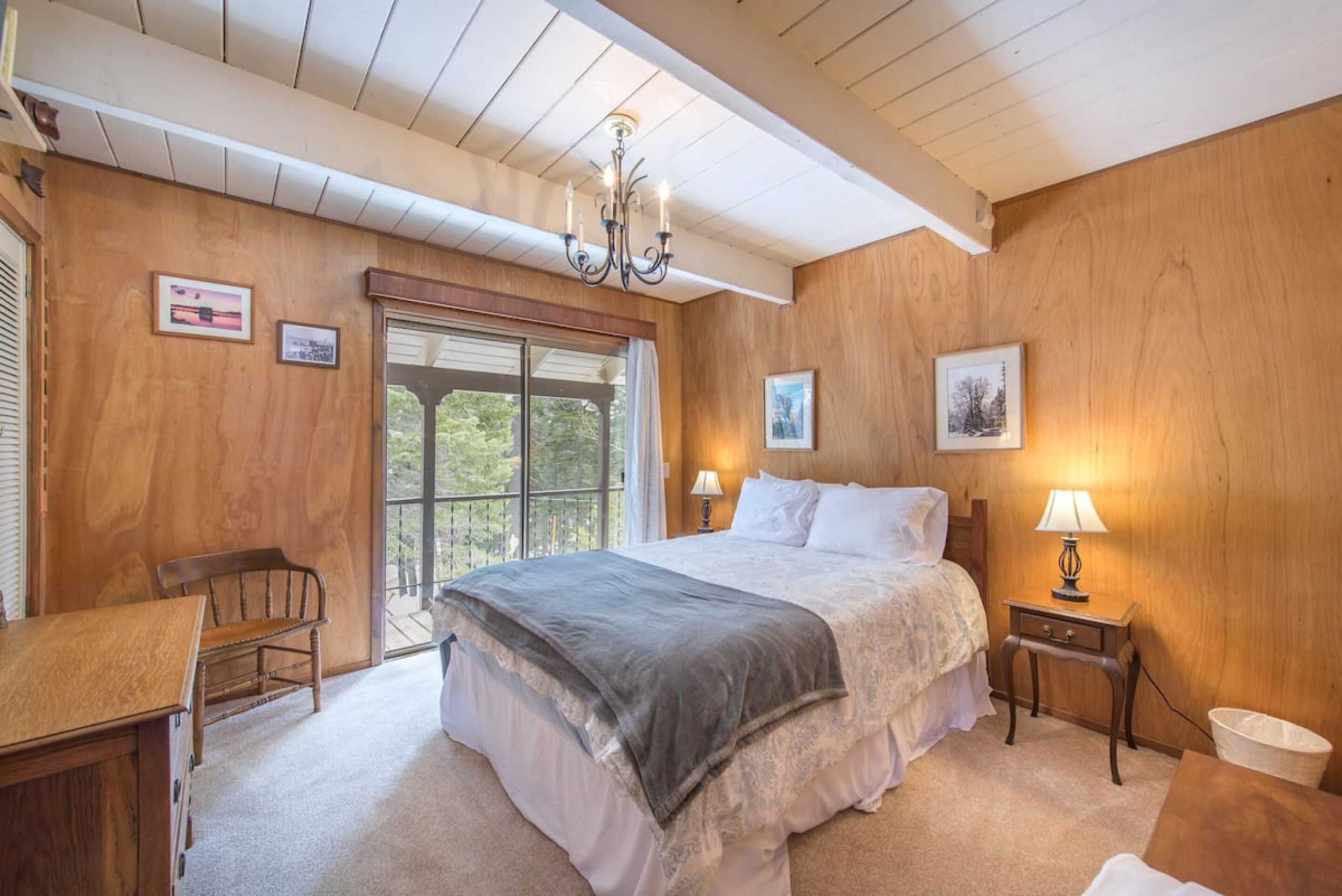 Une chambre à coucher avec un grand lit, des murs en bois, un lustre, un bureau et une fenêtre donnant sur un beau paysage.