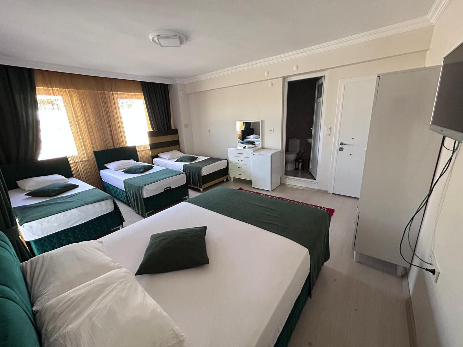 A hotel room with two single beds, a small desk, a mirror, and a television.