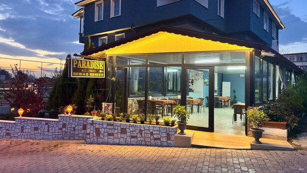 A two-story building with a glass storefront, outdoor seating, and a signboard. - Paradise House  (Denizli)