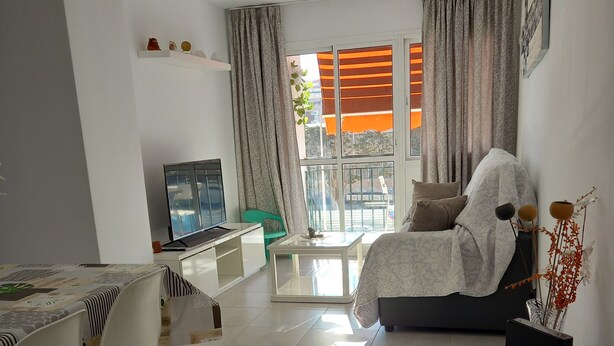 A modern living room with a sofa, a dining table with chairs, a TV, and a balcony with curtains. - Sunny and central terrace apartment (Málaga)