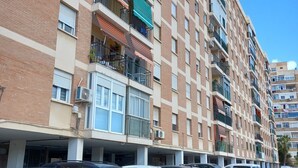 A multi-story residential building with balconies, a parking area with several cars, and a clear blue sky. - Sunny and central terrace apartment (Málaga)