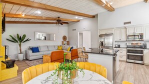 A modern kitchen with stainless steel appliances, a dining area with yellow chairs, and a living room with a gray sofa and a ceiling fan. - Scottsdale Game House Heated Pool, Golf, Bowling (Scottsdale)