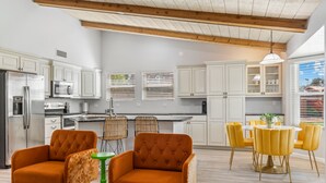 A modern kitchen with white cabinets, a stainless steel refrigerator, and a dining area with yellow chairs and a green table. - Scottsdale Game House Heated Pool, Golf, Bowling (Scottsdale)