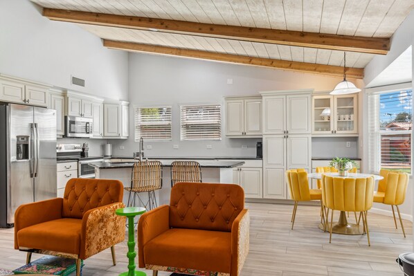 A modern kitchen with white cabinets, a stainless steel refrigerator, and a dining area with yellow chairs and a green table. - Scottsdale Game House Heated Pool, Golf, Bowling (Scottsdale)