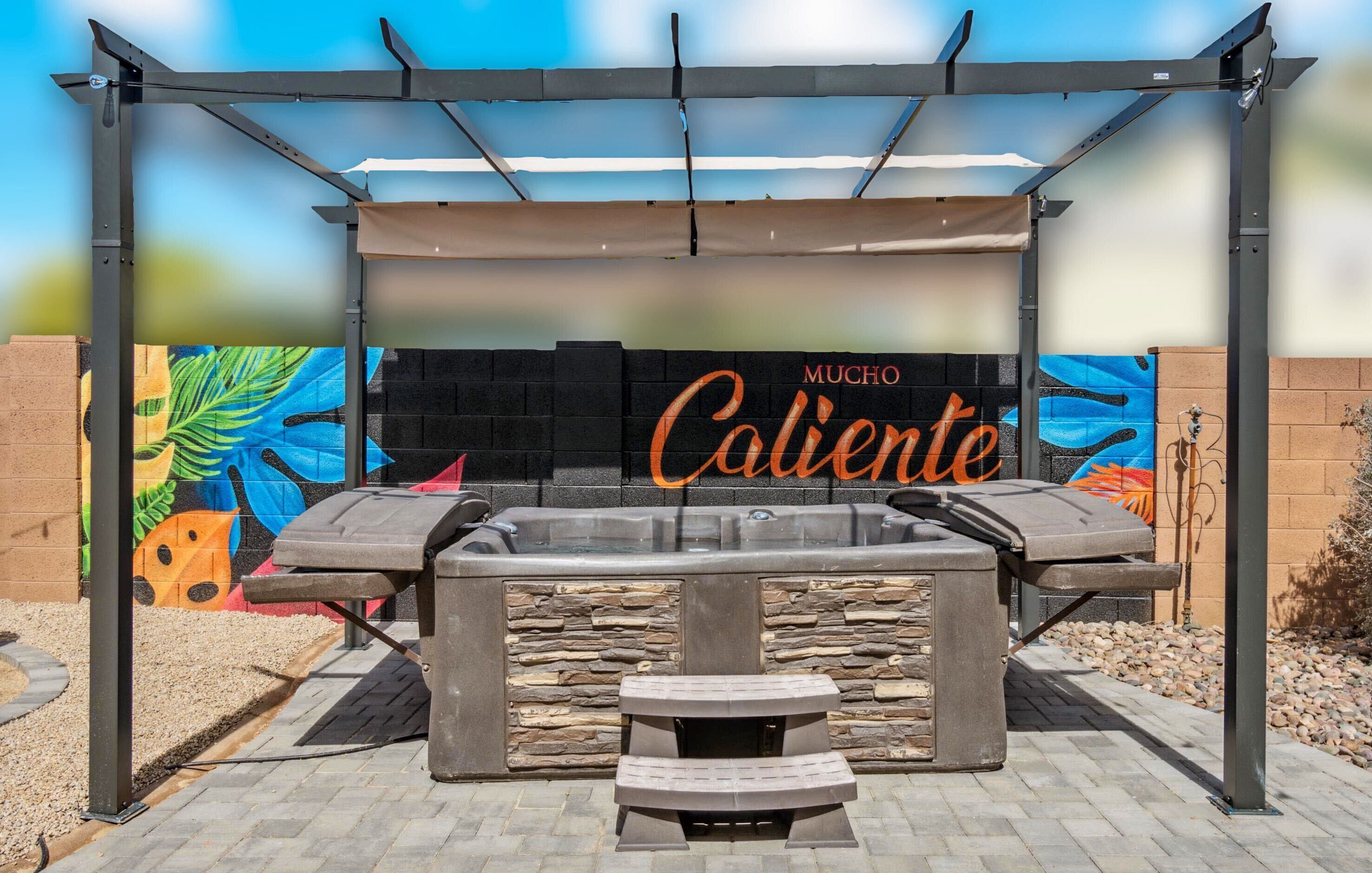 An outdoor seating area with a pergola, a hot tub, and a stone wall with a mural.