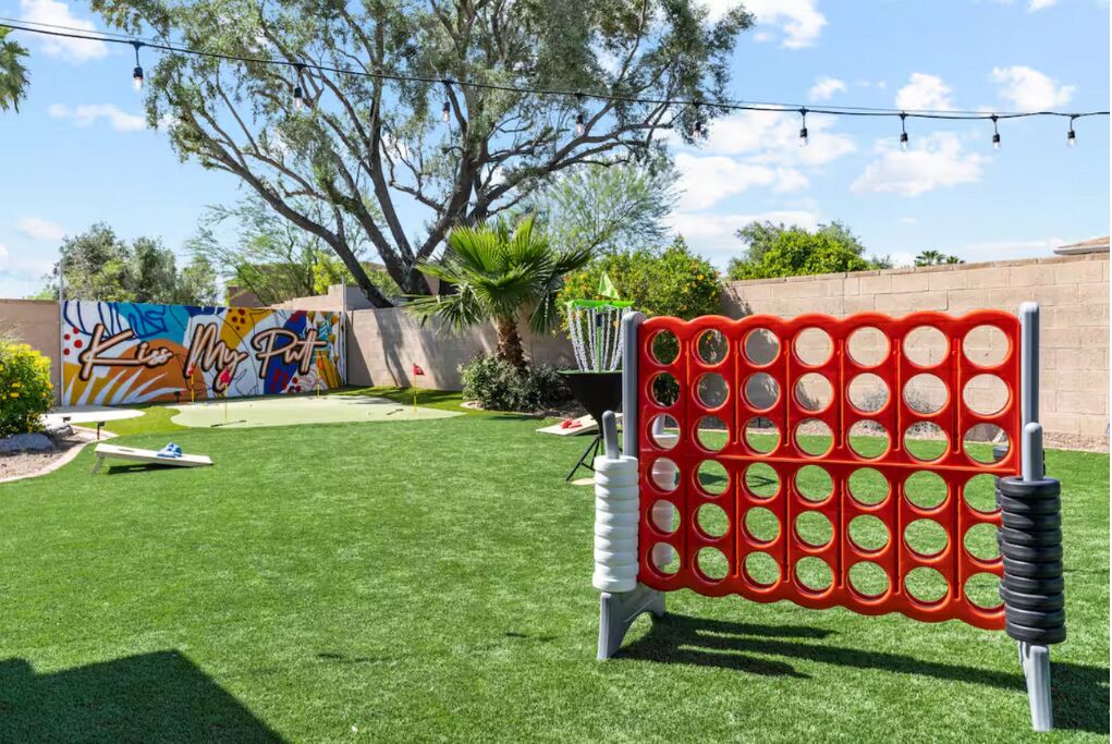 A backyard with a red and white game structure, a mural, and a tree.