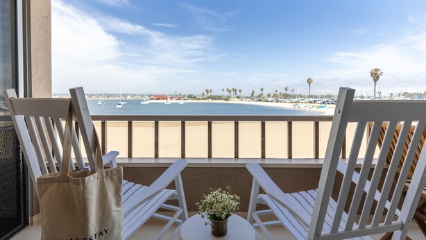 A balcony with white chairs, a small table, and a view of the beach and ocean.