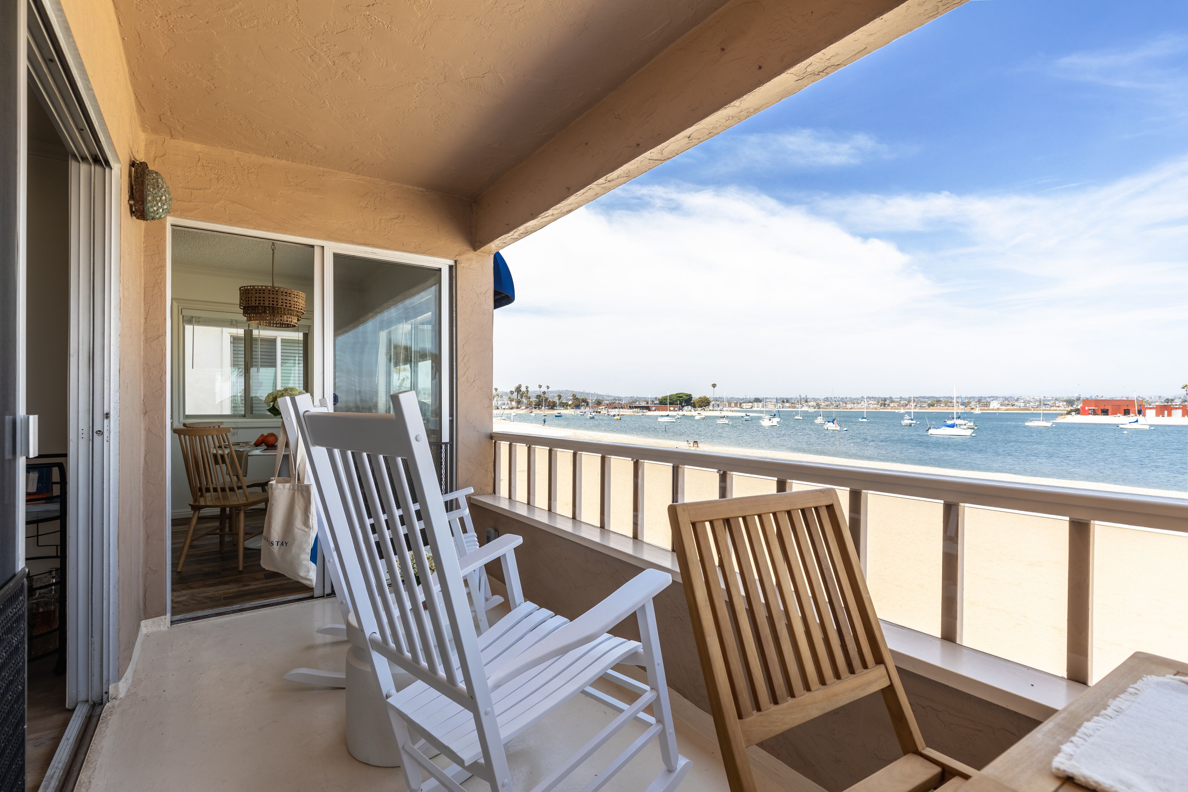 Un balcon avec des chaises blanches, une table et une vue sur la mer, où l’on aperçoit des bateaux.
