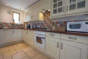 A kitchen with white cabinets, a microwave, a stove, and a window with a clock.