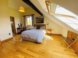 A bedroom with a sloped ceiling, a bed, a desk, a chair, a lamp, and a window.
