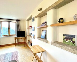 Un salon comprenant un téléviseur, des livres, un banc et des étagères ornées de photos et d’objets décoratifs.