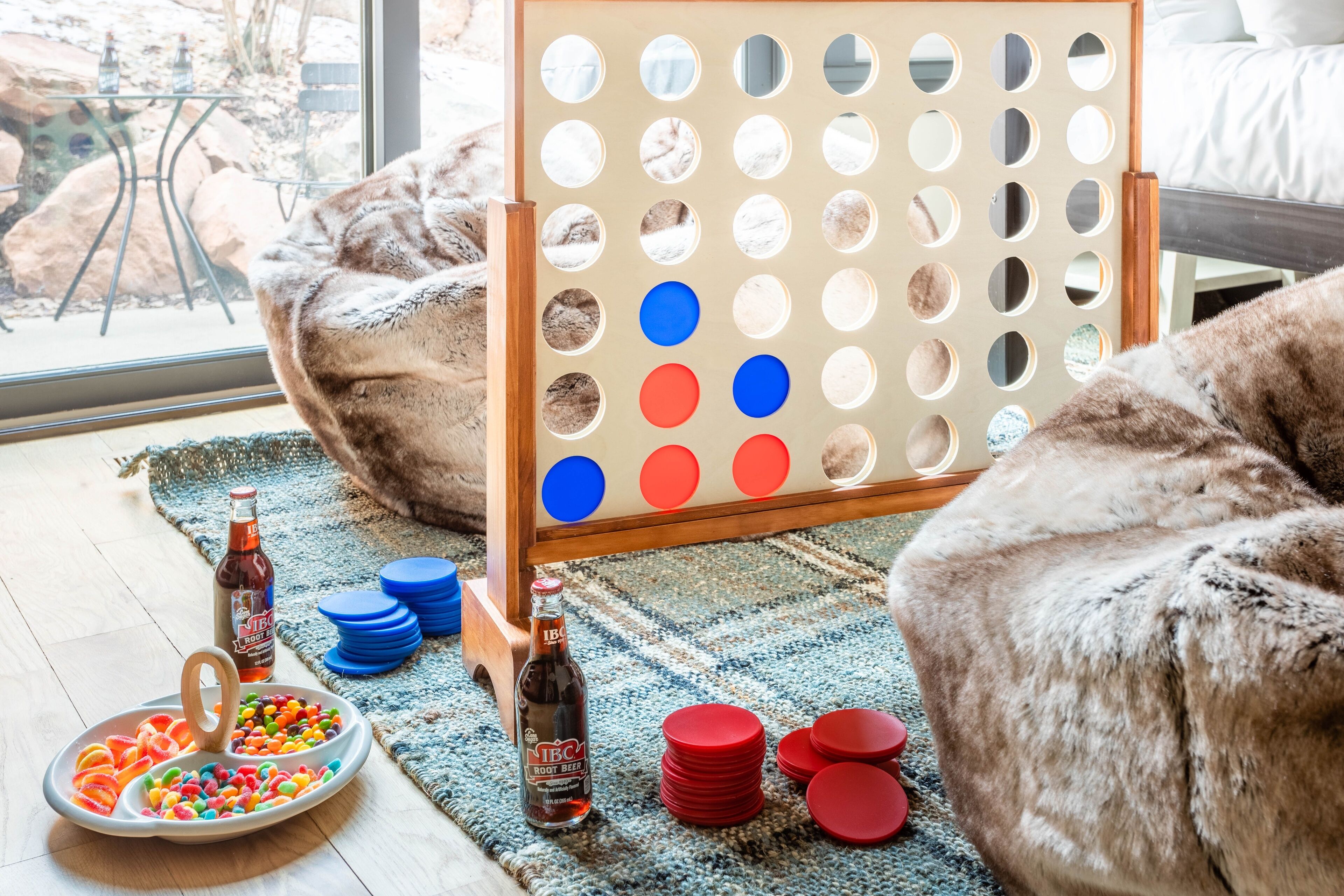 Una habitación acogedora con un ventanal grande, un juego de mesa de madera, un plato de aperitivos y una botella de cerveza.