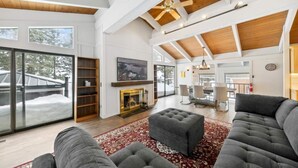 A spacious living room with a fireplace, large windows, and a high ceiling with exposed beams. - Lake View Treasure -  Luxury with Lake Views (Incline Village)