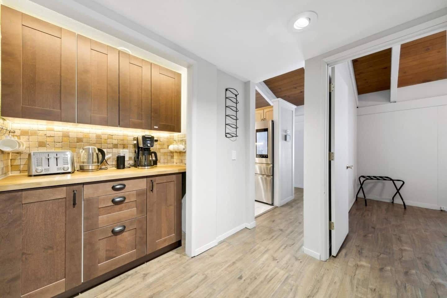A modern kitchen with wooden cabinets, a countertop with a toaster and coffee maker, and a hallway leading to a dining area.