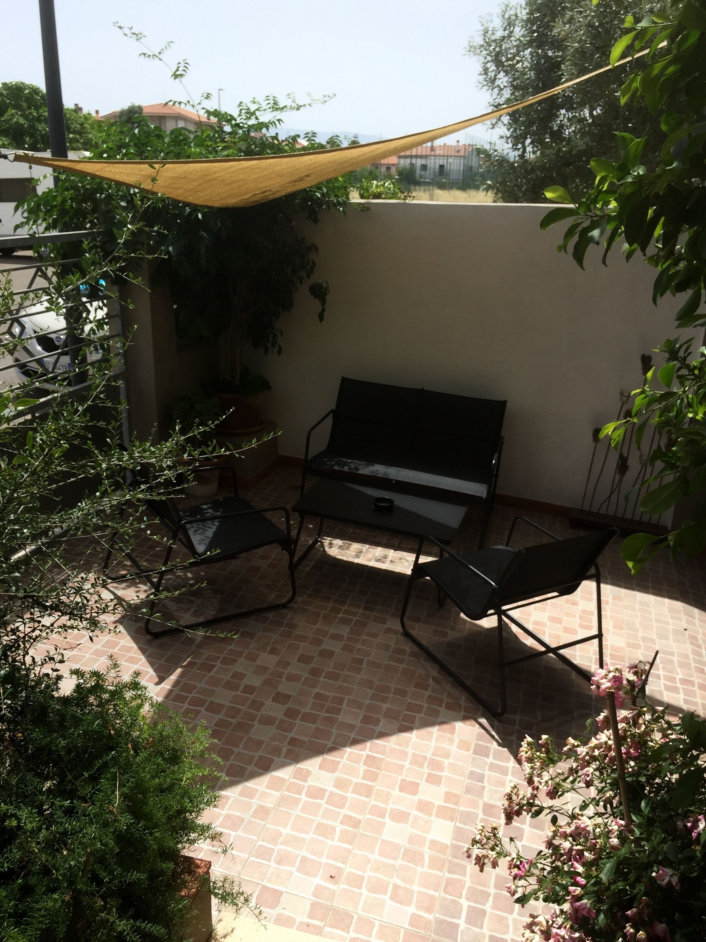 A patio area with a black sofa, two chairs, a small table, and a potted plant.
