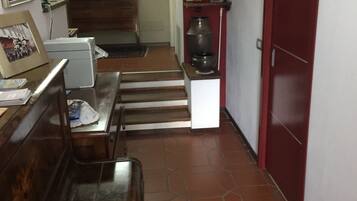 A hallway with a staircase, a desk with papers, a printer, framed pictures on the wall, and a red door.