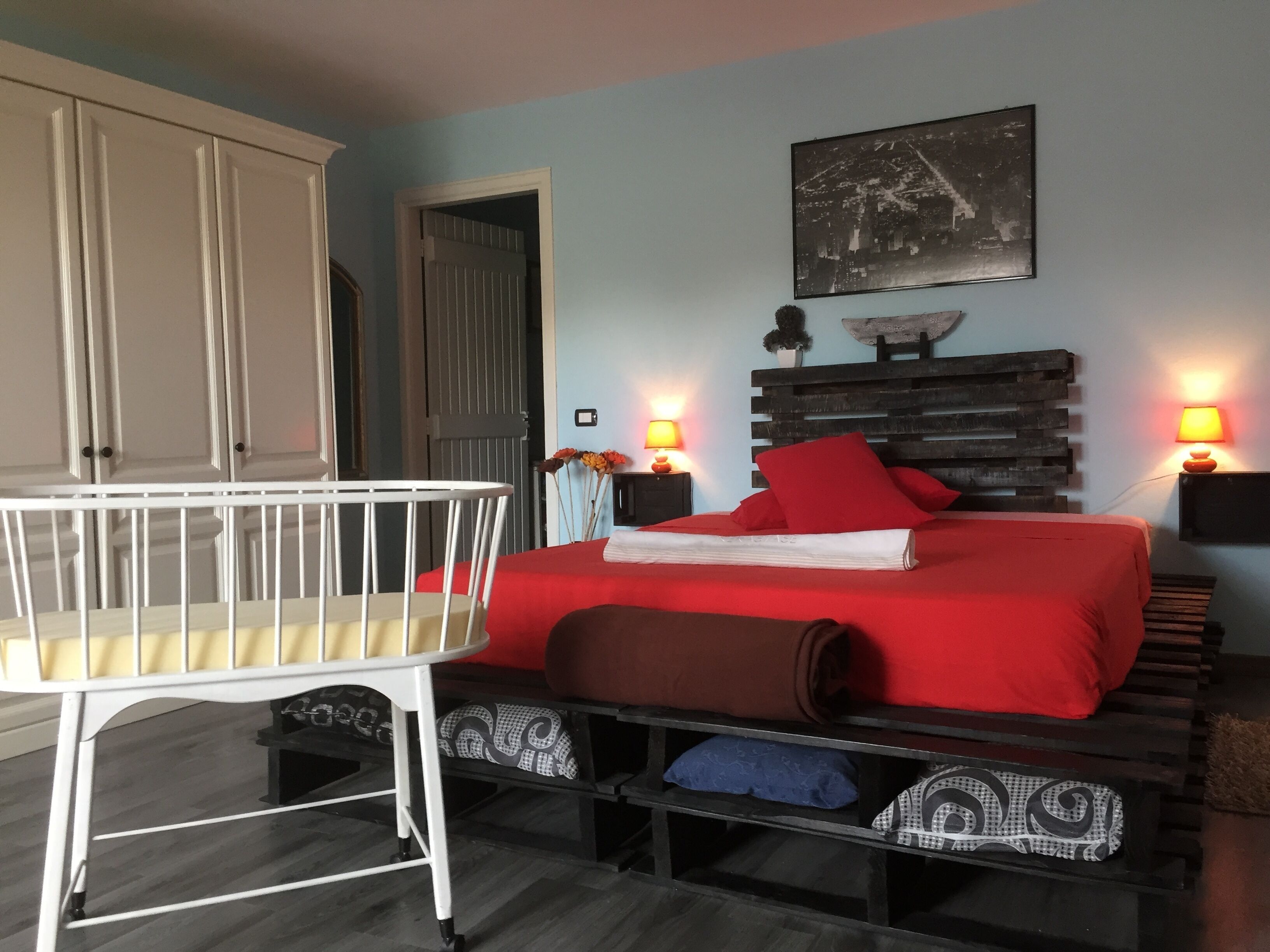 Une chambre à coucher avec un lit, des lampes de chevet, un berceau et une étagère fixée au mur.